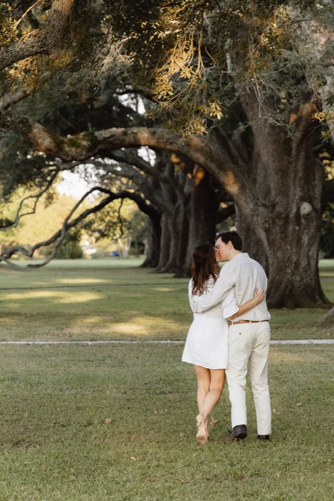 Couple walking under large oak trees in New Orleans park.