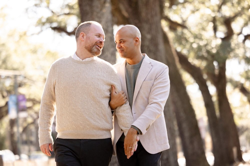 Two men walking together outdoors in New Orleans, smiling and holding hands.