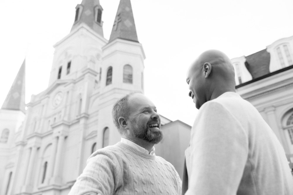Two men smiling and talking outdoors in front of a church in New Orleans.