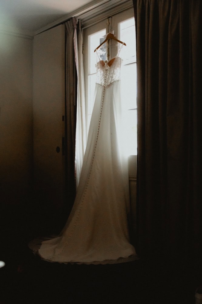 Elegant wedding dress hanging in front of a window with curtains, ready for a New Orleans wedding.