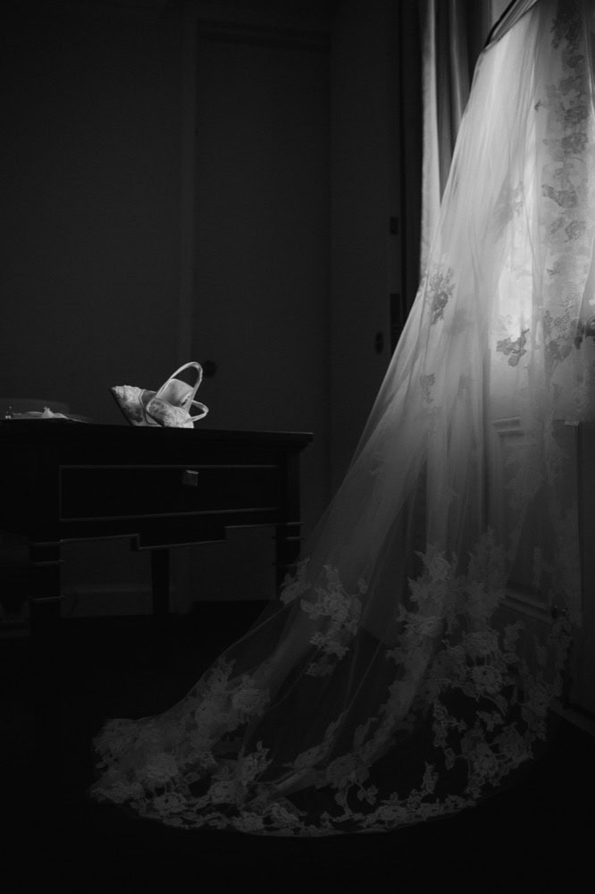 Wedding dress hanging by the window with lace details and flowing fabric.