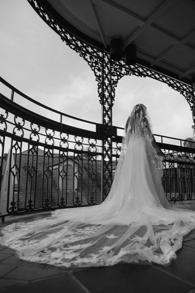 Bridal gown with long train draped over balcony railing in black and white.