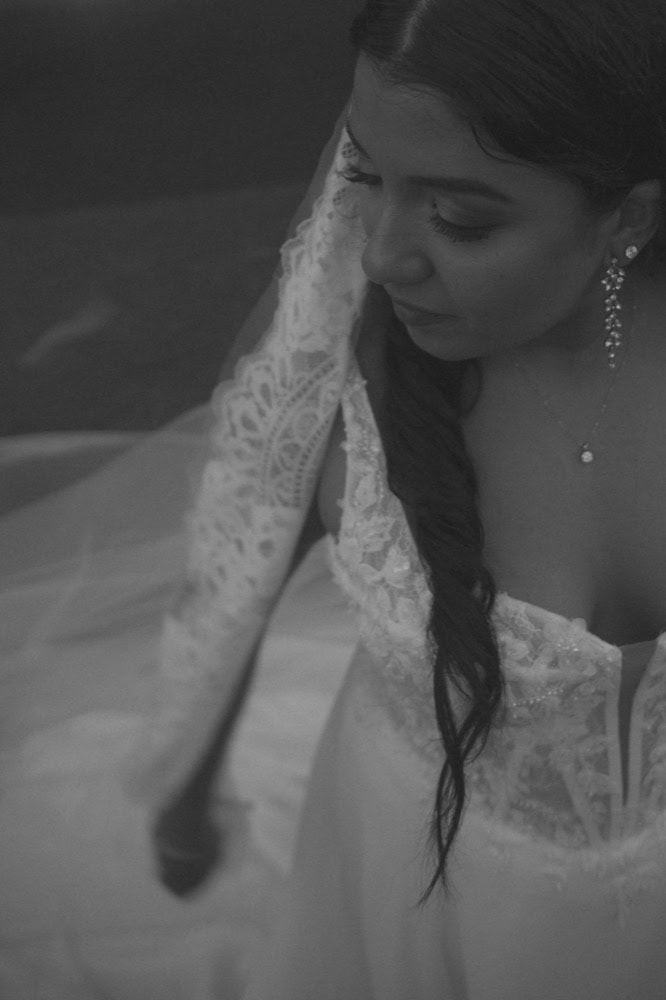 Elegant bride in lace wedding dress with earrings and necklace, looking down thoughtfully.