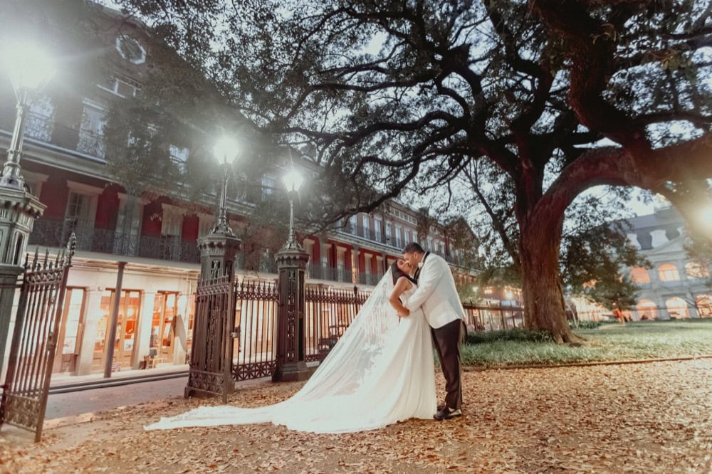 Elegant New Orleans wedding couple embracing under a large oak tree at dusk, with historic architect.