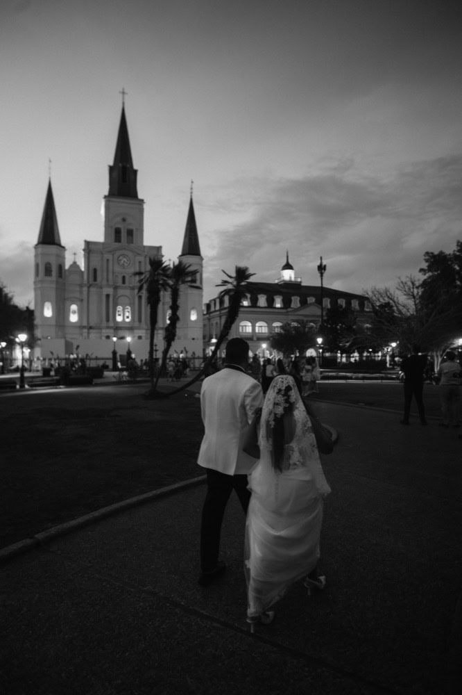 Couple walking hand-in-hand in front of St. Louis Cathedral during sunset in New Orleans.