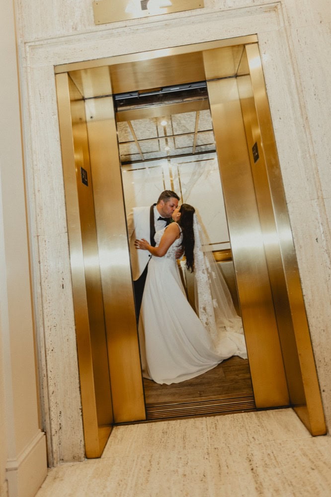 Elevator doors open to reveal a bride and groom sharing a romantic kiss inside.