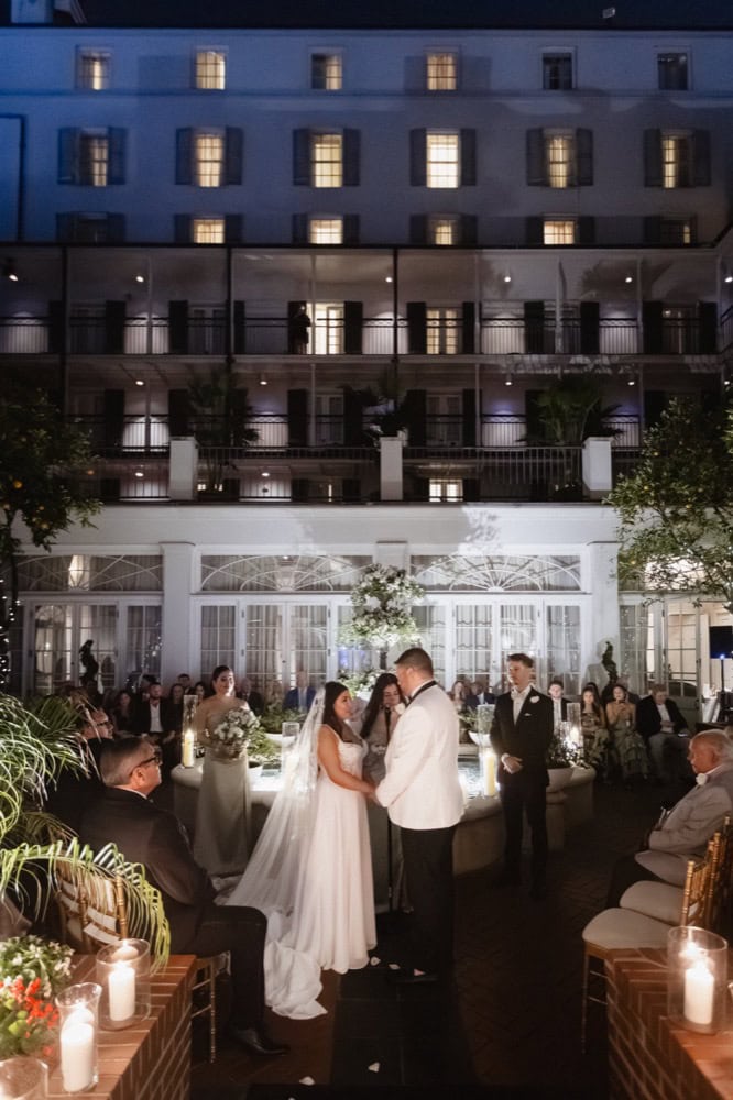 Romantic wedding ceremony outdoors at night in a beautifully lit courtyard, with guests and a couple.