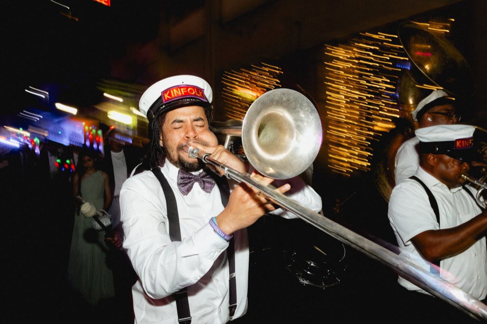 Jazz musician playing trombone at a lively New Orleans event with colorful lights.