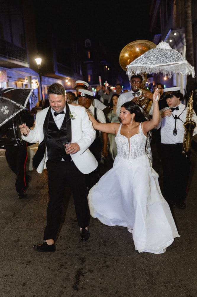 Joyful bride and groom dancing during a lively New Orleans wedding parade at night.