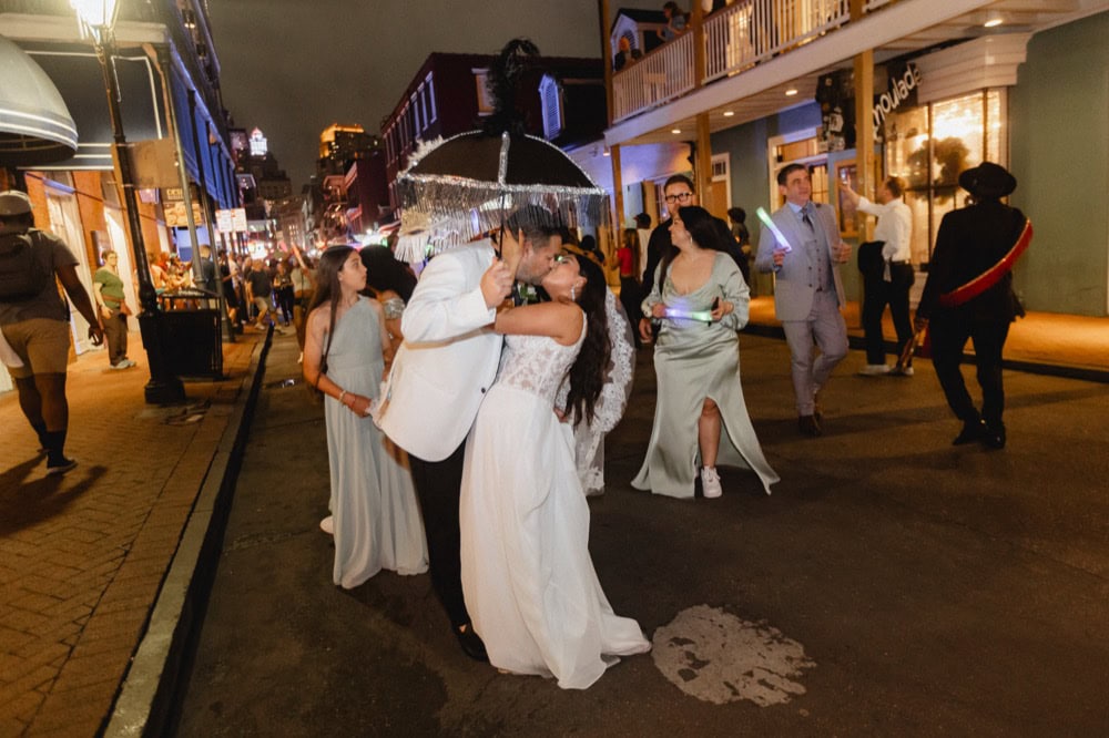 Wedding couple kissing under an umbrella on a lively city street at night.