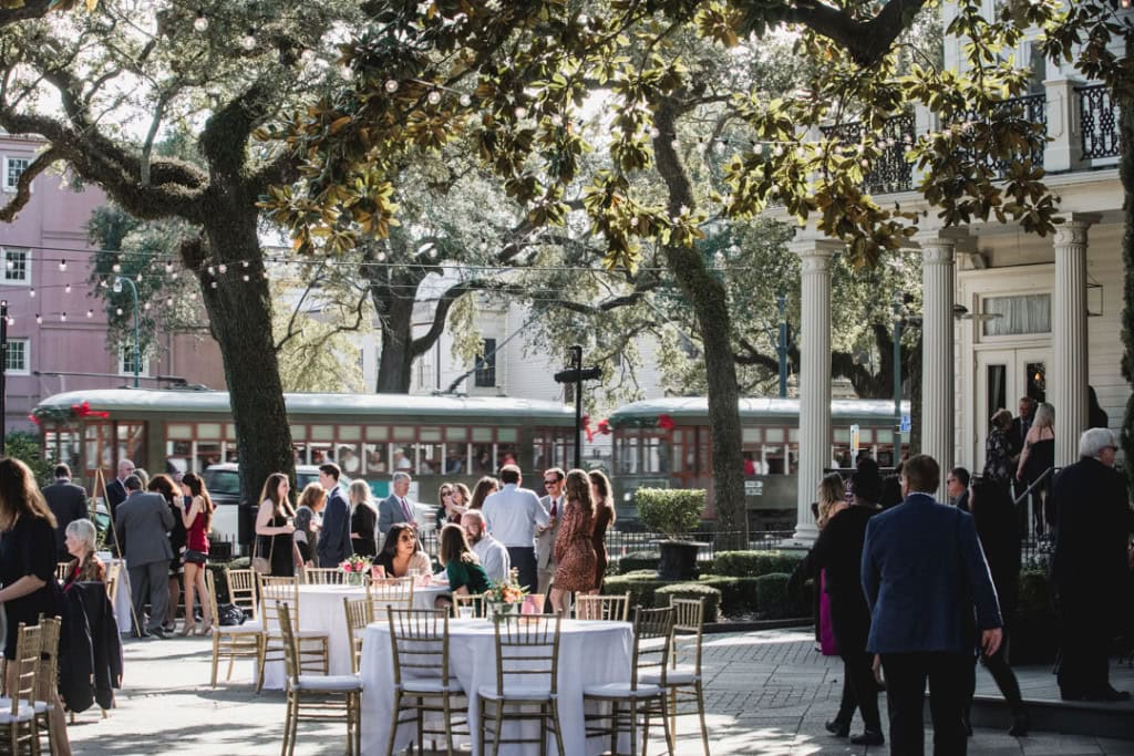 Wedding reception in New Orleans with outdoor tables and guests under large trees.