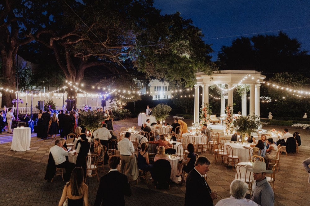 Outdoor wedding reception at night with string lights and guests.