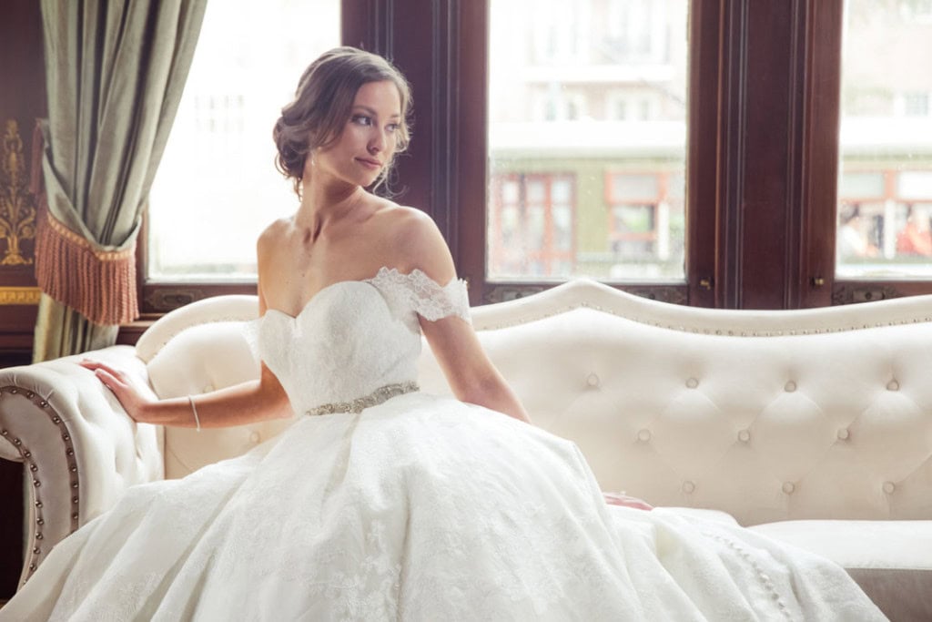 Bride in wedding dress sitting on vintage sofa by window in New Orleans.