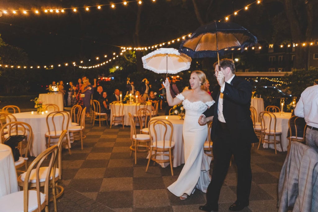 Bride and groom dancing under umbrellas at outdoor wedding reception.