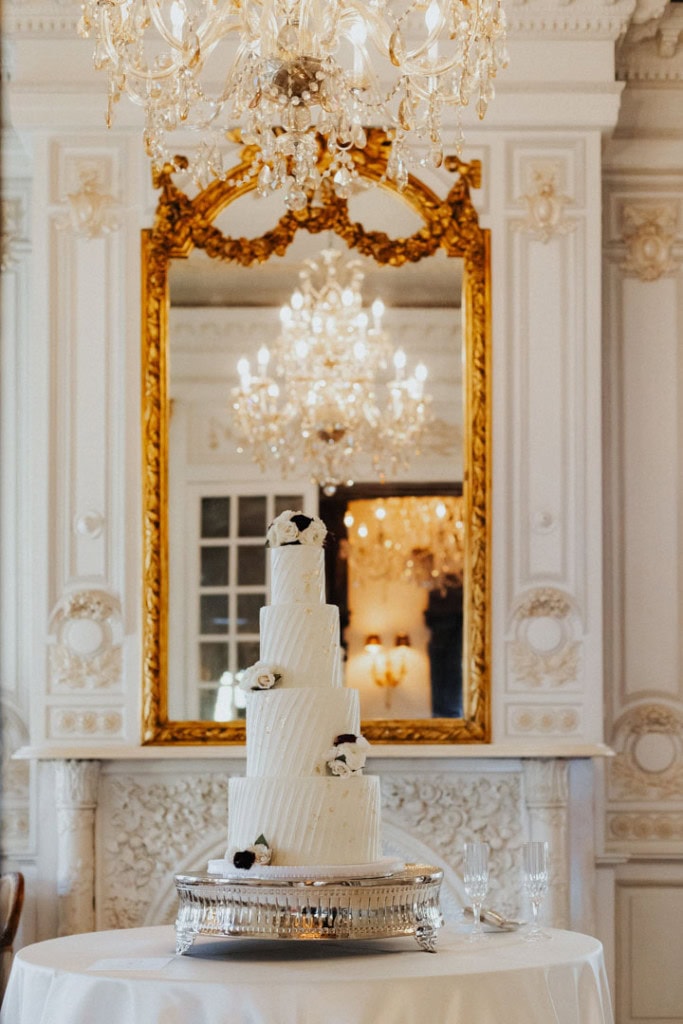 Wedding cake with white roses and black accents in luxurious ballroom.