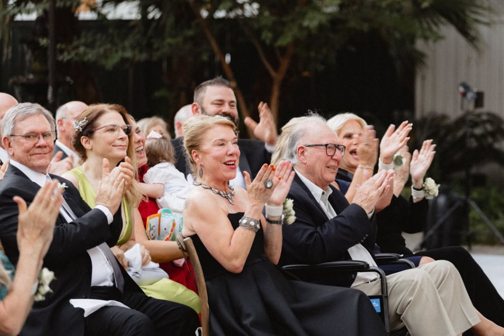 Guests at a New Orleans wedding celebrating and clapping outdoors.