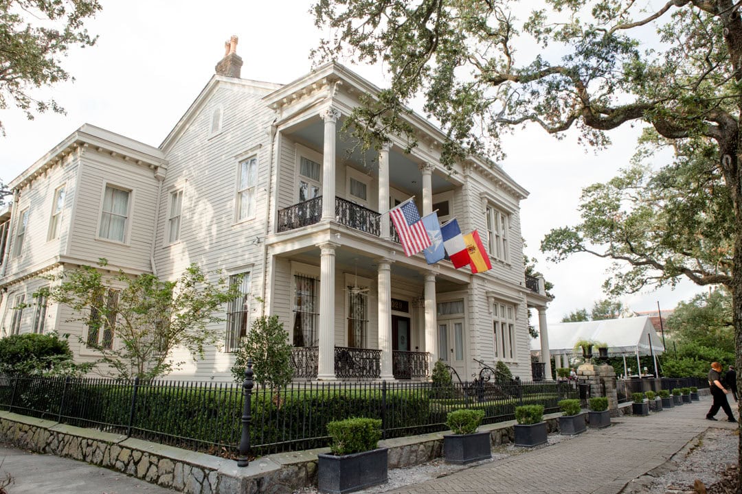 Elegant historic house in New Orleans with flags and lush greenery.