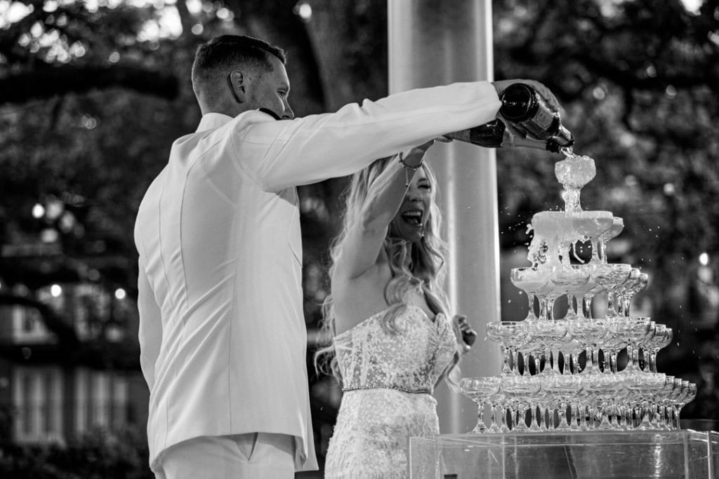 Groom and bride pouring champagne on wedding cake in New Orleans.