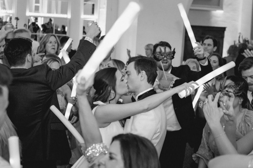 Couple kissing at wedding reception with guests and celebration.