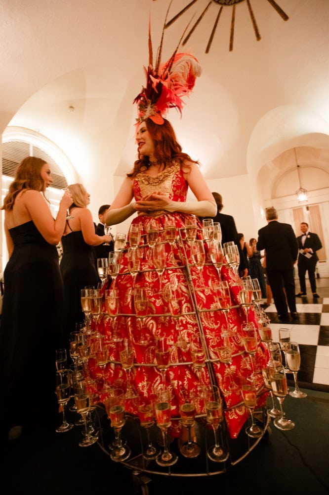 Champagne Woman in elaborate red gown with feathered headpiece at wedding reception.