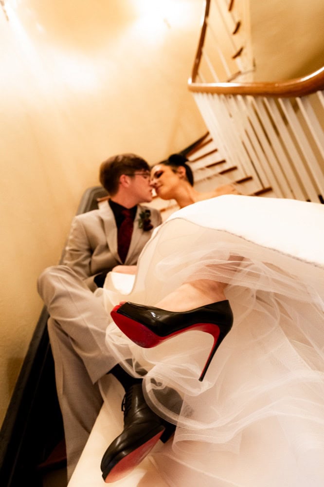 Bride and groom sharing a kiss on staircase with bride's high heel visible.
