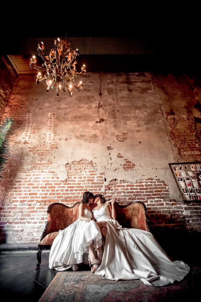 Two brides sitting on vintage sofa a Latrobe's on Royal wedding venue with chandelier.