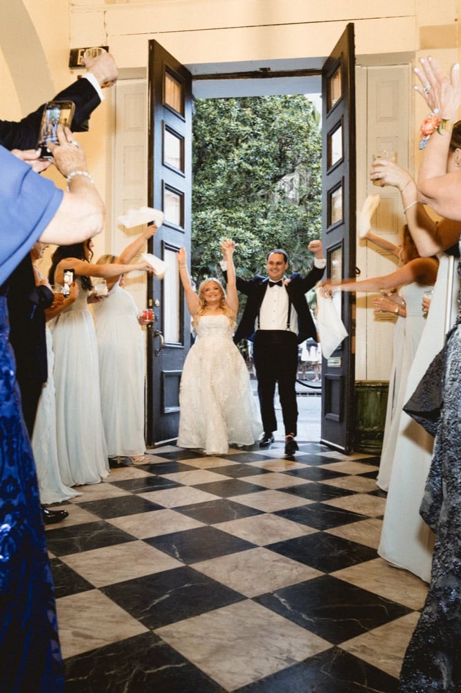 Bride and groom entering wedding venue with guests cheering and taking photos.