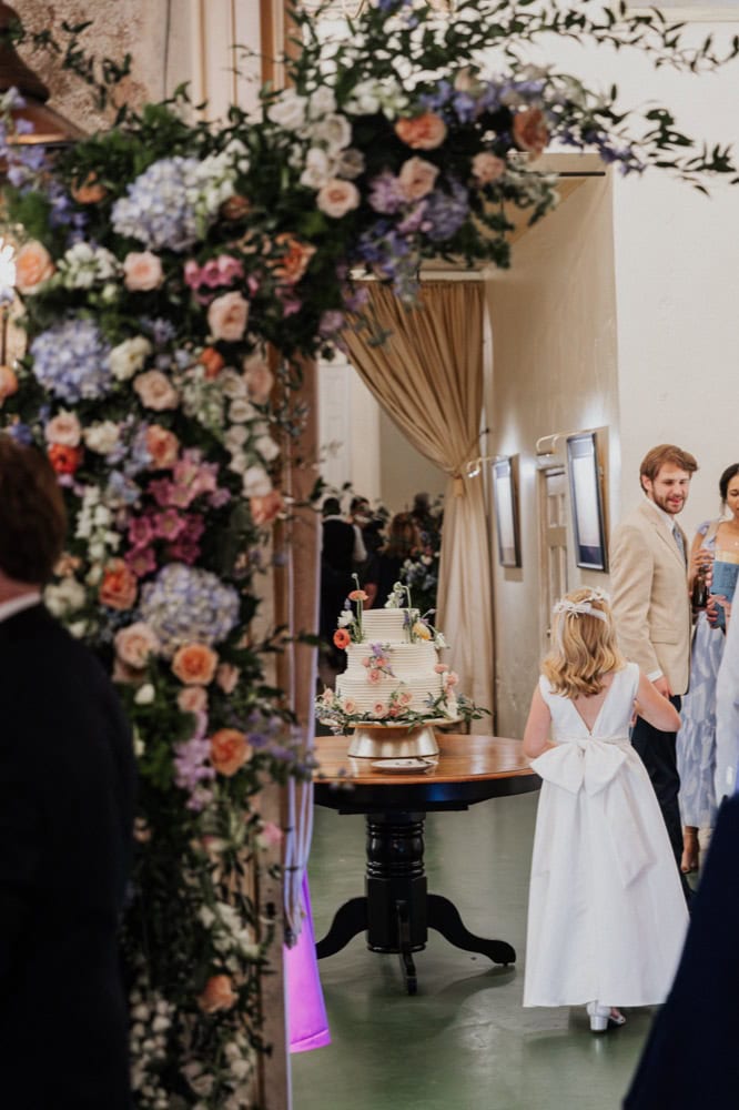 Wedding reception scene with floral arch, cake, and guests in New Orleans venue.