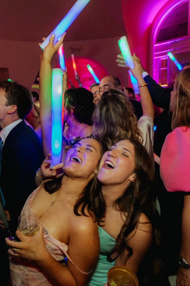 Joyful wedding guests dancing with glow sticks at New Orleans event.