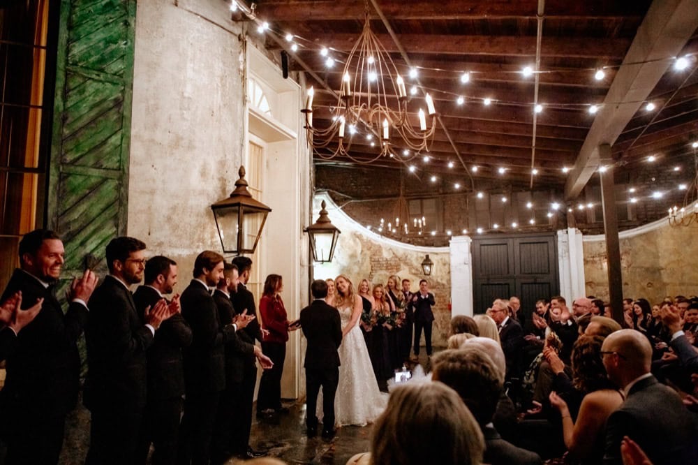 Wedding ceremony in a rustic venue with string lights and guests.