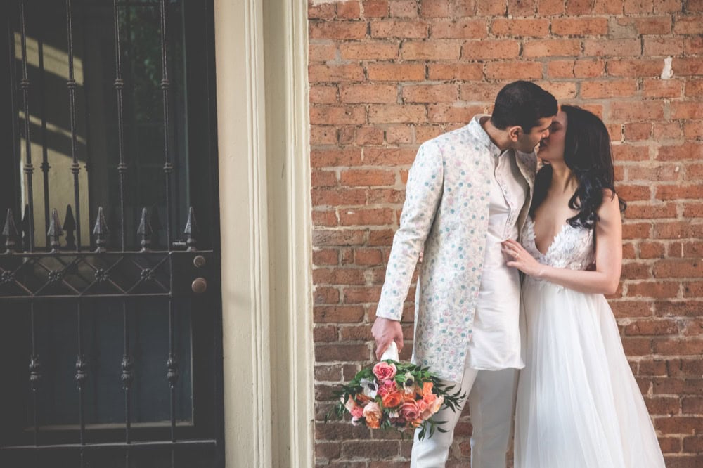 Couple kissing outside with wedding dress and floral bouquet.