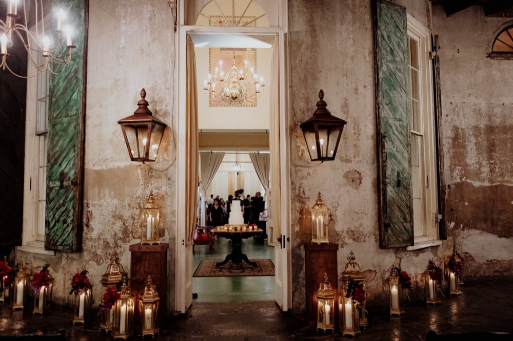 Wedding cake in the center of a room at Latrobe's on Royal as seen through French Doors flanked by gas lanterns.