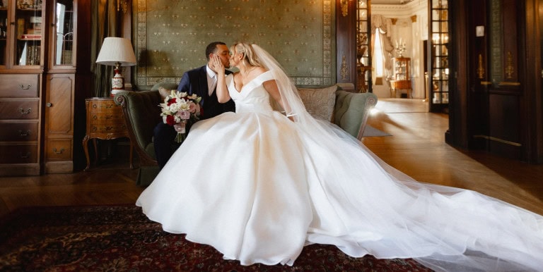Bride and groom sharing a kiss in an elegant historic room.