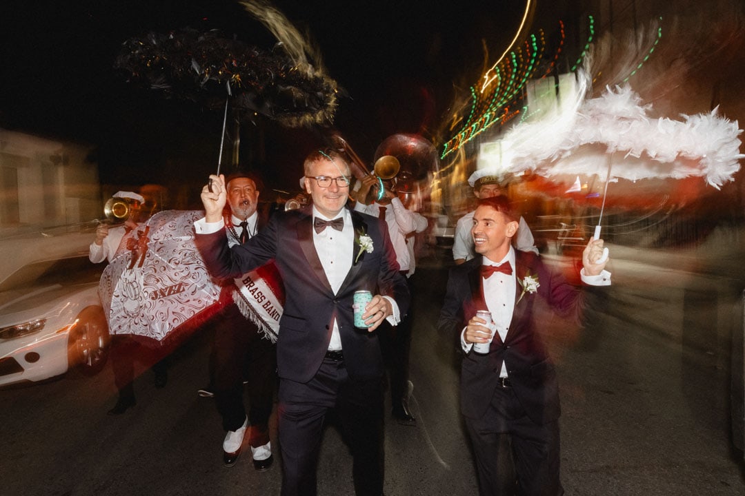 Wedding celebration in New Orleans with grooms holding umbrellas during a second line parade at night.