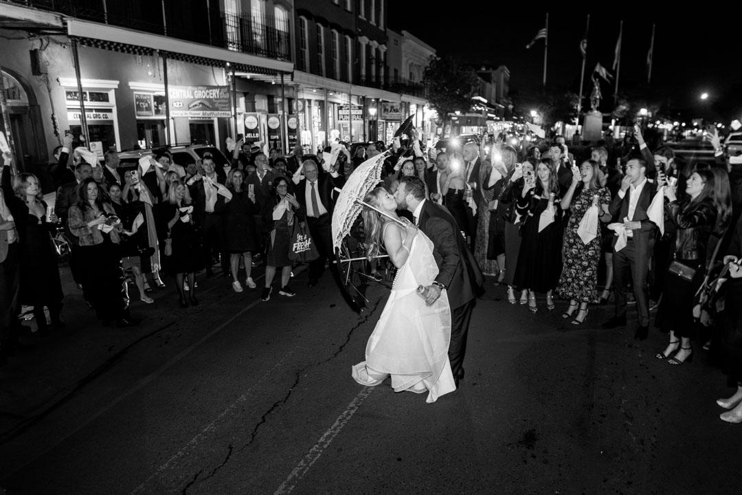 Wedding couple dancing under umbrellas in the street during their second line parade in New Orleans at night.