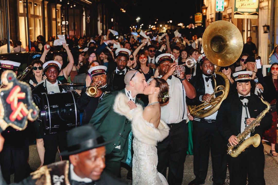 Wedding couple kissing during lively New Orleans second line parade with band.
