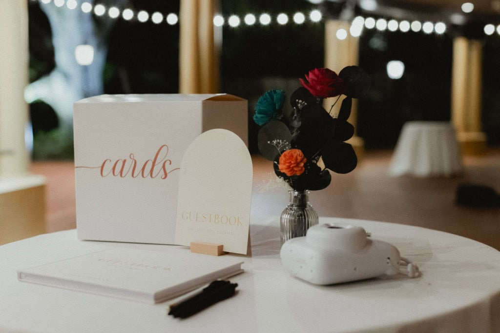 Wedding guest book, cards, and floral arrangement on table at reception.