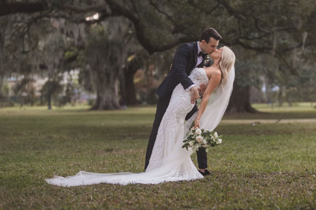 Bride and groom kissing outdoors in wedding attire at Audubon Park in New Orleans.