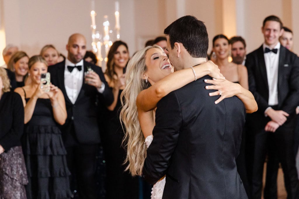 Bride and groom dancing at wedding reception with guests in background.