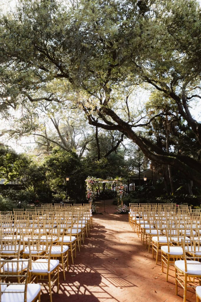 Beautiful outdoor wedding setup with chairs and floral arch under large trees at the Audubon Tea Room.