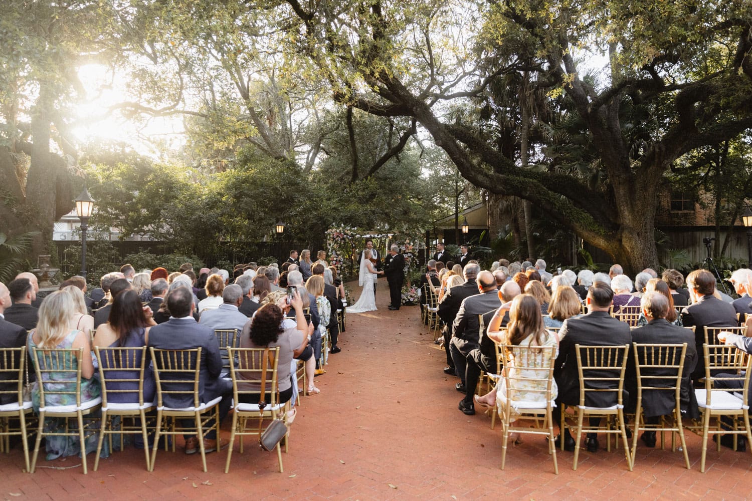 Beautiful outdoor wedding ceremony at the Audubon Tea Room in New Orleans with guests seated under large oak trees.