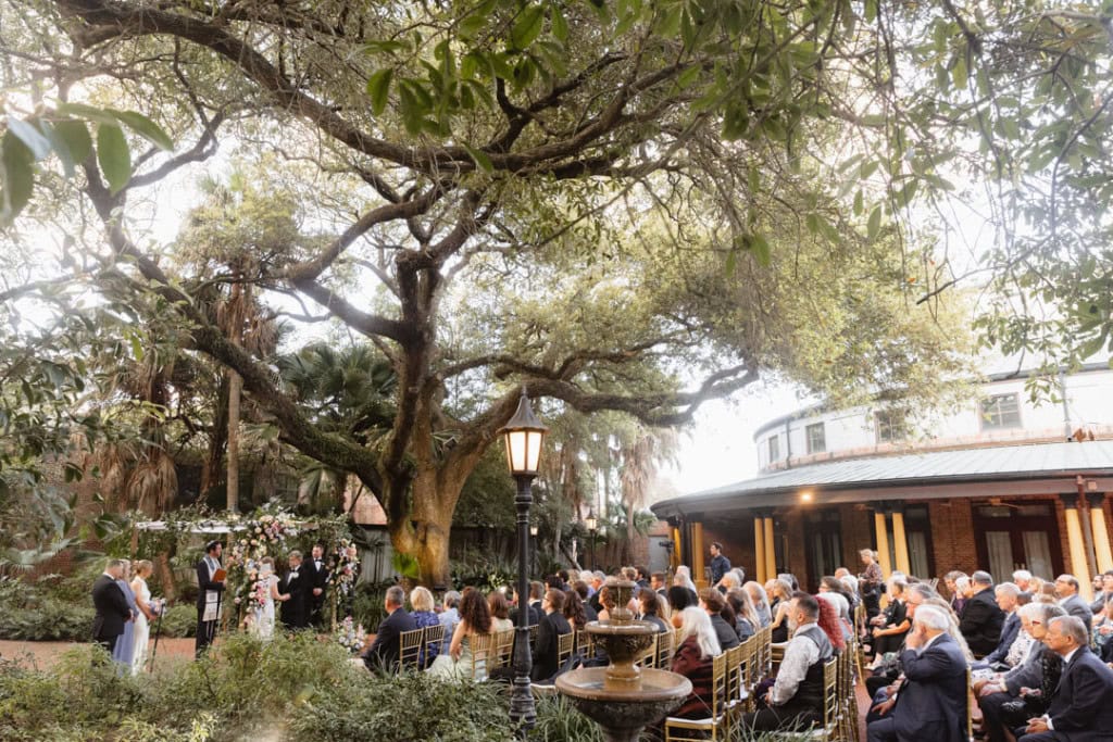 Wedding ceremony outdoors under large tree at the Audubon Tea Room in New Orleans with guests seated.