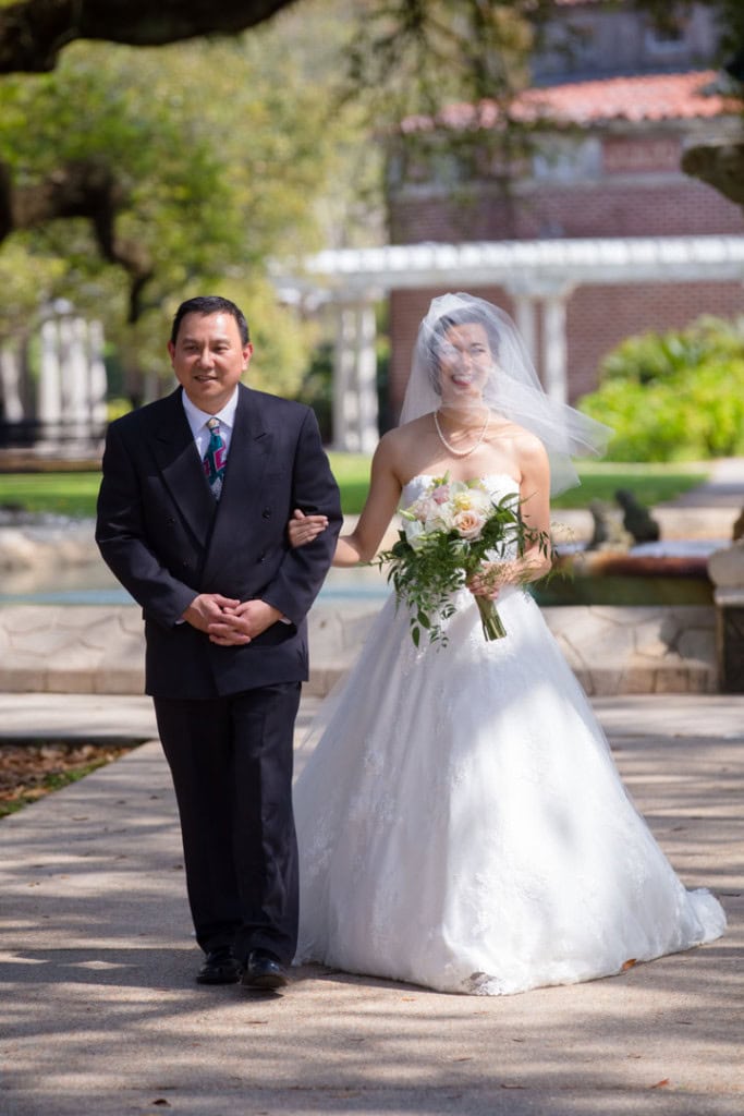Bride walking with father in New Orleans park during wedding ceremony.