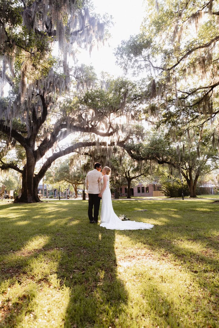 Bride and groom under large oak tree in New Orleans park.