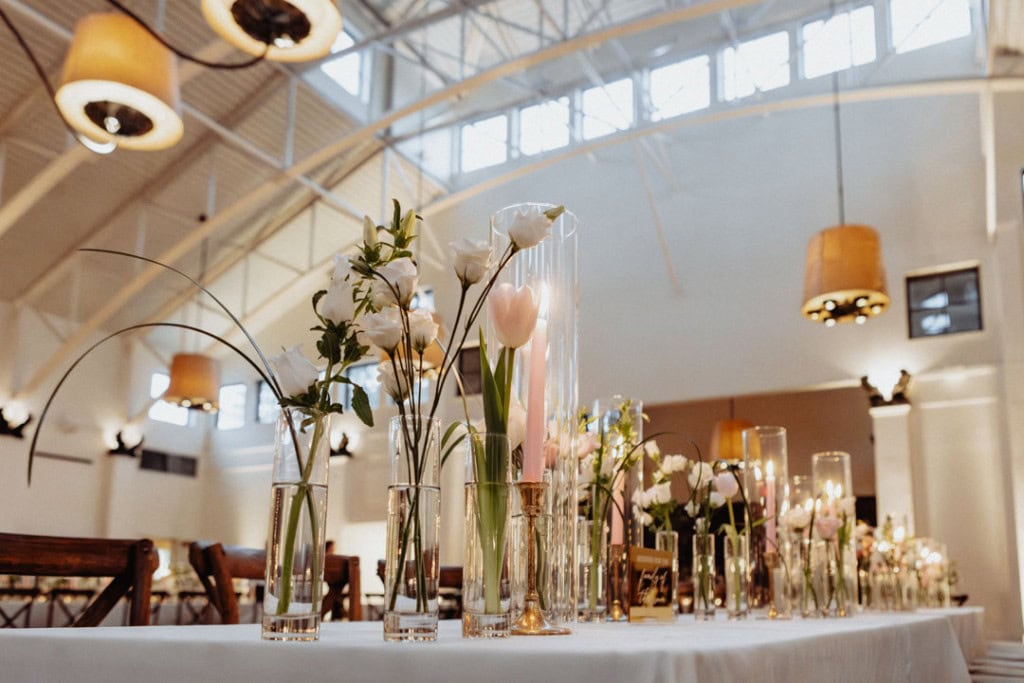 Small vases of pink and white flowers candles on display on table tops inside the Audubon Tea Room at a wedding in New Orleans.