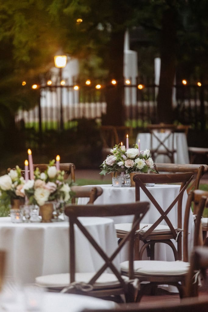 Bouquets of pink and white flowers with light pink candles on display on table tops outside of a wedding in New Oreans.