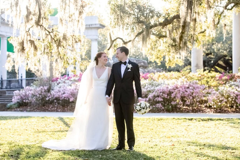 Bride and groom holding hands at the Audubon Zoo during wedding in New Orleans, pink and white flowering azaleas behind them.